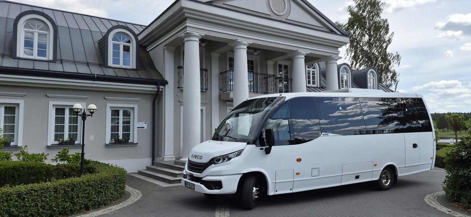 Biały minibus Iveco Wing ARTRANS przed dworkiem